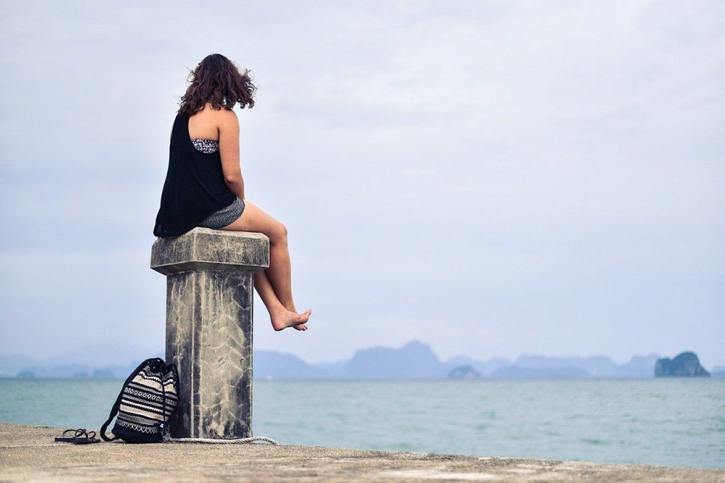 Frau sitzt allein am Hafen und schuat aufs Meer.